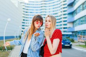 fechar acima verão retrato do dois mulheres rindo e engasgar ao ar livre em a rua. urbano fundo foto