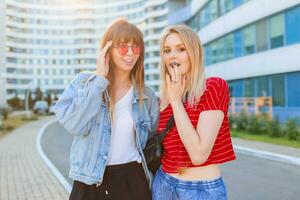 fechar acima verão retrato do dois mulheres rindo e engasgar ao ar livre em a rua. urbano fundo foto