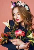 lindo jovem fêmea com grandes ondulado Loiras cabelo dentro guirlanda do Primavera flores posando com flor ramalhete sobre Rosa fundo. foto