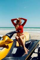 jovem sexy loiro mulher com perfeito corpo dentro vermelho equipamento sentado em água lambreta em a de praia dentro uma luz do sol. verão final de semana ou período de férias. extremo esporte. foto