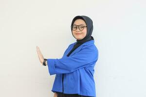 lindo jovem ásia muçulmano mulher, vestindo óculos e azul blazer mostrando Pare gesto enquanto sorridente foto