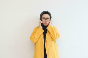 retrato do lindo ásia mulher dentro hijab, óculos e vestindo amarelo blazer fazer telefone ligar com fofa face expressão foto