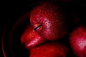 Suculenta maçã vermelha fresca com gotas de água contra um fundo escuro