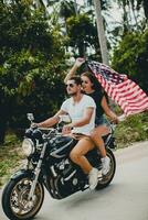 jovem casal dentro amor, equitação uma motocicleta, abraço, paixão, livre espírito, americano bandeira foto