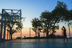 Preto homem fazendo Esportes, jogando basquetebol em nascer do sol, silhueta foto