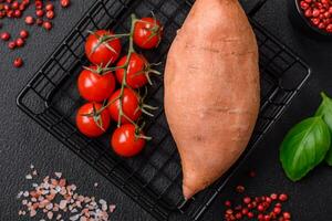 fresco ampla Rosa doce batata tubérculos com tomates e especiarias em uma Sombrio fundo foto