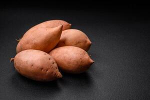 fresco ampla Rosa doce batata tubérculos com tomates e especiarias em uma Sombrio fundo foto