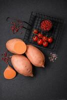 fresco ampla Rosa doce batata tubérculos com tomates e especiarias em uma Sombrio fundo foto