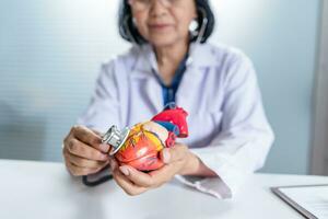 cardiologista apoia a coração Senior ásia mulher médico vestindo óculos e uniforme. retrato do maduro velho ásia mulher médico profissional foto