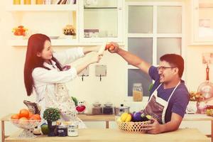 casal asiático na cozinha brincando um com o outro com legumes foto