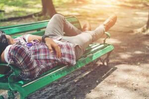 homem jovem hippie deitado no banco do parque verde, olhando para longe. foto