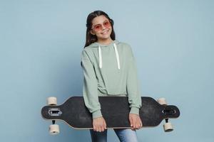 garota linda e positiva de óculos escuros segurando um skate nas mãos foto