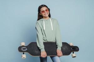 garota linda e positiva de óculos escuros segurando um skate nas mãos
