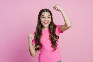 menina adolescente se alegra com sua vitória em um fundo rosa foto