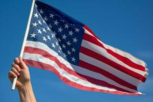 uma fechar-se do uma veterano mão segurando a americano bandeira, com uma pano de fundo do uma Claro azul céu, representando patriotismo e honra. generativo ai foto