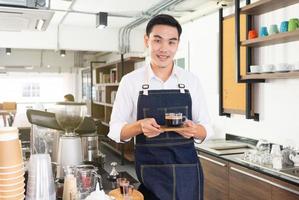 jovem barista asiático prepara café expresso quente para servir o cliente no café foto