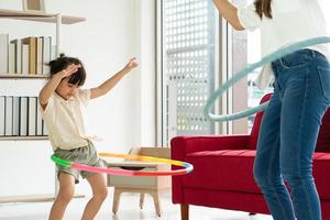 criança asiática brincando de bambolê com a mãe na sala de estar no verão foto