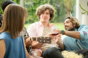 multiétnico grupo do amigos tendo Diversão jogando guitarra e cantando juntos às casa foto