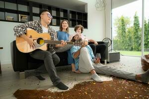 multiétnico grupo do amigos tendo Diversão jogando guitarra e cantando juntos às casa foto