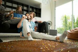 multiétnico grupo do amigos tendo Diversão jogando guitarra e cantando juntos às casa foto