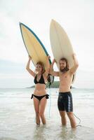 jovem homem e mulher segurando pranchas de surf em seus cabeças e andar para dentro a mar para surfar foto