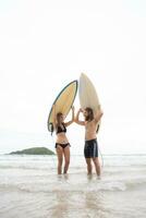 jovem homem e mulher segurando pranchas de surf em seus cabeças e andar para dentro a mar para surfar foto