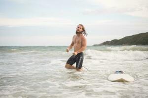 retrato do uma bonito jovem homem com prancha de surfe às a de praia foto