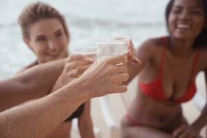 multiétnico grupo do amigos tendo Diversão em a praia, bebendo Cerveja e tendo Diversão foto