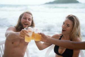 multiétnico grupo do amigos tendo Diversão em a praia, bebendo Cerveja e tendo Diversão foto