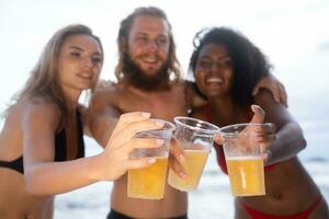 multiétnico grupo do amigos tendo Diversão em a praia, bebendo Cerveja e tendo Diversão foto