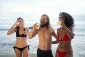 multiétnico grupo do amigos tendo Diversão em a praia, bebendo Cerveja e tendo Diversão foto
