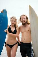 casal do surfistas segurando pranchas de surf em a de praia. homem e mulher dentro Preto maiôs. foto