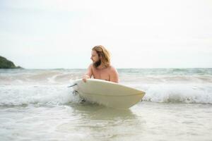 jovem homem surfar em a de praia tendo Diversão e balanceamento em a prancha de surfe foto