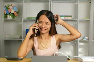 mulher trabalhando às casa usar seu telefone e computador para comunicar com seu companheiros de equipe. foto