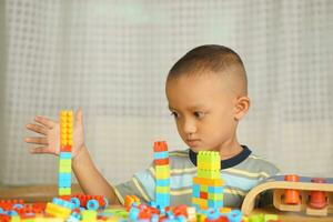 ásia Garoto jogando com educacional brinquedos lá estão muitos lindo cores em a mesa dentro a casa. foto