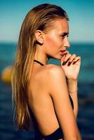 atraente jovem mulher com perfeito bronzeado em forma corpo posando em a de praia contra azul céu. vestindo roupa de banho , molhado cabelo, natural faço acima. foto