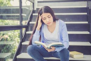 mulher asiática lendo livro, estudando para os exames com cansaço.
