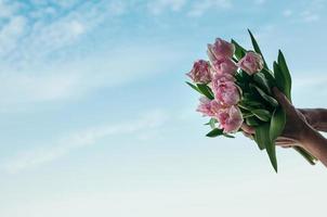 um buquê de flores rosa em uma mão contra o fundo do céu azul foto