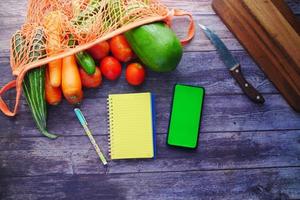 legumes frescos, tábua de cortar, bloco de notas e telefone inteligente na mesa foto