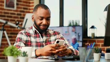 feliz alegre pessoa conversando com conectados amigos sobre a telefone, desfrutando ele mesmo dentro acolhedor à moda lar. entretido africano americano homem rolagem em dele social meios de comunicação alimentar, portátil trabalho de câmera foto