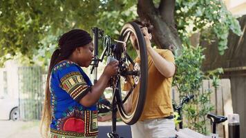 ativo motivado interracial casal lado de fora ajustando bicicleta roda com profissional equipamento. jovem Preto mulher agarrando especializado Ferramentas para ajudar caucasiano homem dentro fixação bicicleta. foto
