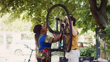 jovem entusiasmado caucasiano homem e africano americano mulher realizando manutenção em bicicleta rodas Como ao ar livre verão passatempo. multiétnico casal fixação bicicleta pneu com profissional equipamentos. foto