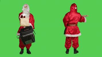 entregador dentro vermelho santa terno carregando mochila com pizza caixa e papel saco ordem, Natal véspera Entrega conceito. jovem homem santo usuario personagem contra cheio corpo tela verde pano de fundo. foto