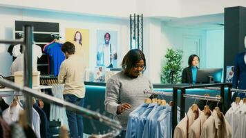 africano americano menina verificação conectados mercado estoque às shopping center, usando Smartphone para Veja às na moda Novo mercadoria. jovem mulher comprador examinando Novo moda coleção, pequeno o negócio conceito. foto