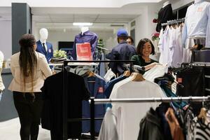 feliz sorridente empregados preparando roupas loja para Preto Sexta-feira vendas, visual comerciante trabalhando dentro moda boutique durante feriado temporada, arranjo com desconto roupas em cabides antes abertura foto