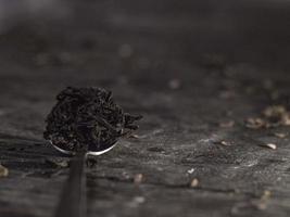 colher de chá cheia de folhas de chá em uma mesa de madeira. chá preto em uma colher. foto