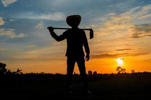 fazendeiro segurando uma enxada em um campo ao pôr do sol foto