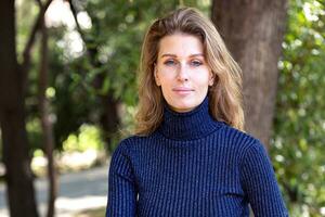 retrato do jovem mulher dentro azul suéter sentado em Banco dentro uma parque foto