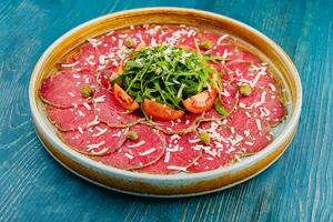 carne carpaccio com alcaparras, parmesão, Rúcula e tomates foto