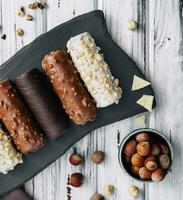 francês sobremesa eclairs ou profiteroles com diferente chocolate gelo em uma Preto pedra prato foto